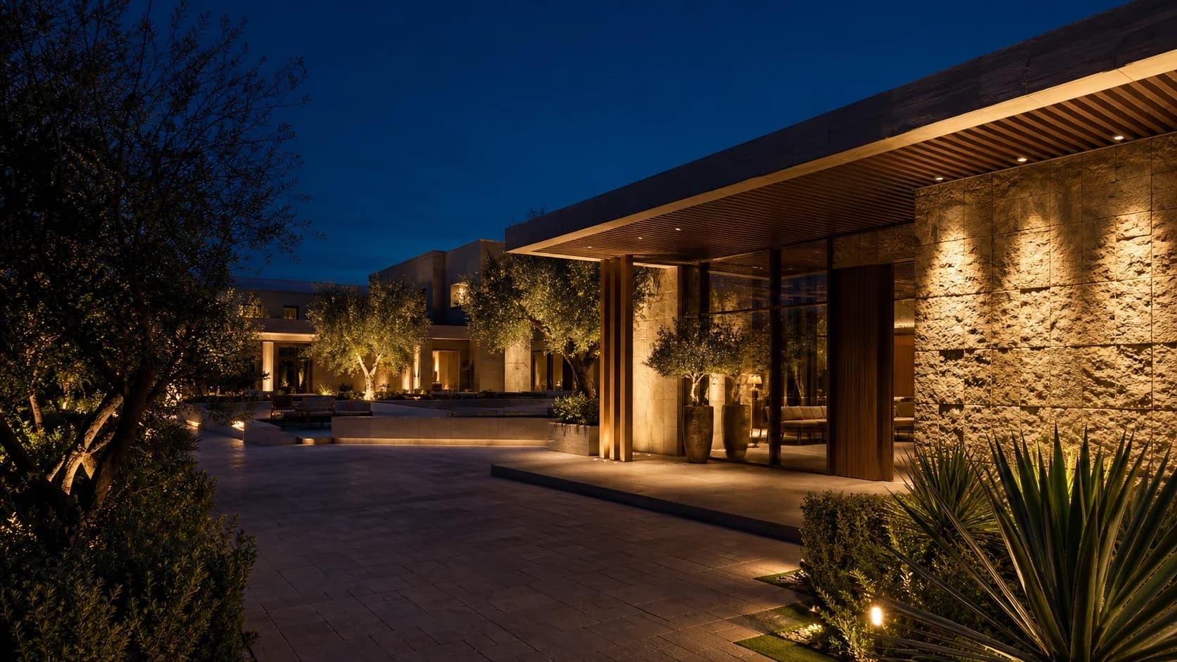 Contemporary Middle East hospitality arrival with integrated facade, interior and landscape lighting at blue hour