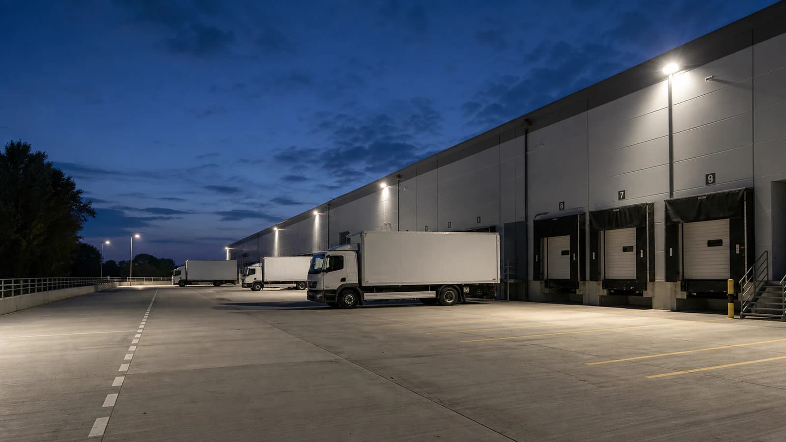 Illustrative LED floodlighting across a logistics loading yard at blue hour